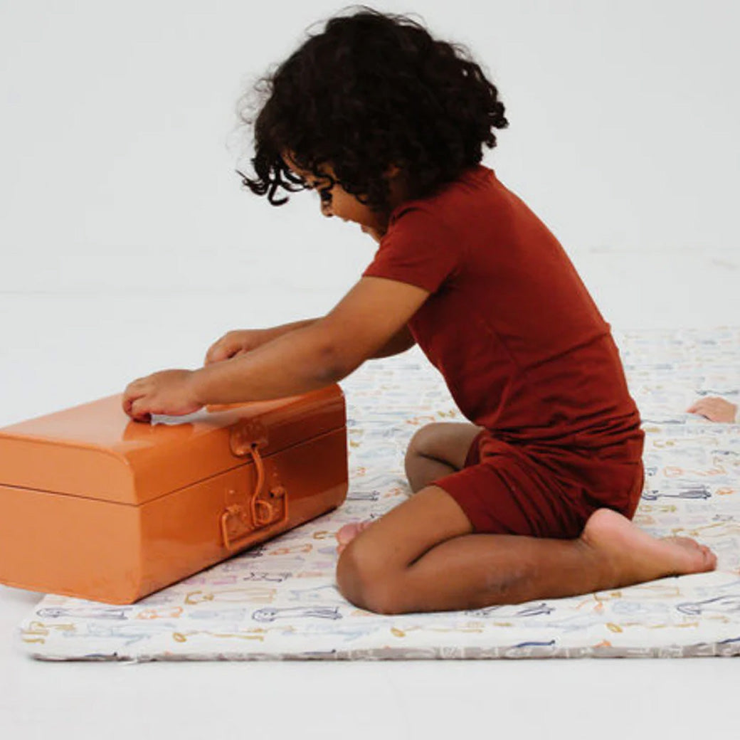 A child playing with a box on the Toki Mats Padded Organic Cotton Play Mat in -- Color_Dogs