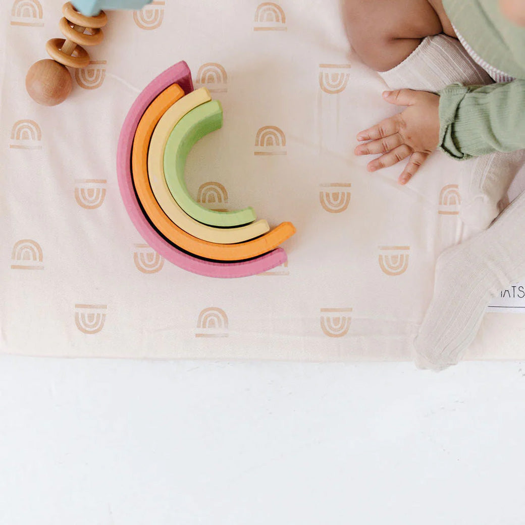 Baby with rainbow toy on the Toki Mats Padded Organic Cotton Play Mat in -- Color_Rainbow Cream