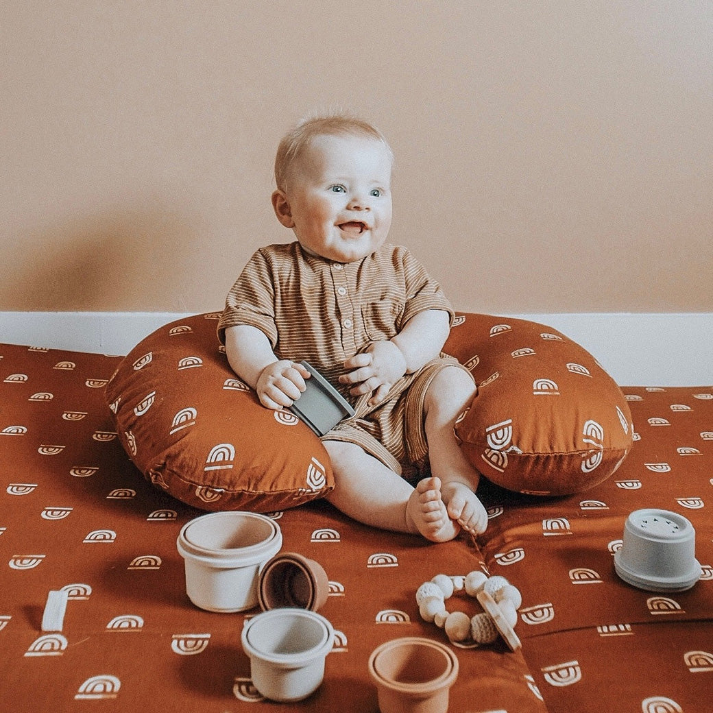 Baby sitting and laughing on the Toki Mats Padded Organic Cotton Play Mat in -- Color_Rainbow Rust