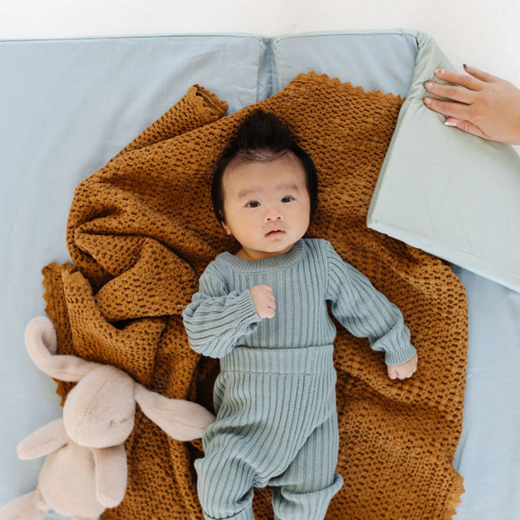Baby laying on a blanket on the Toki Mats Padded Organic Cotton Play Mat in -- Color_Sage + Breeze