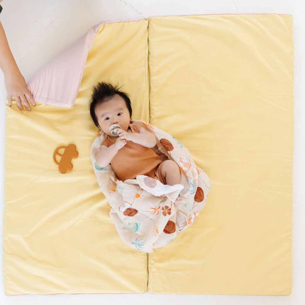Baby laying on the Toki Mats Padded Organic Cotton Play Mat with some toys in -- Color_Tutu + Daisy
