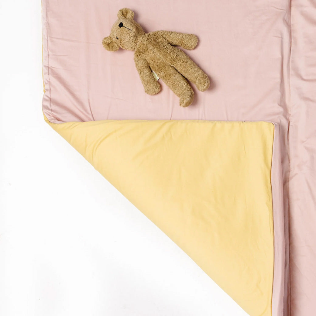A teddy bear toy on top of the Toki Mats Padded Organic Cotton Play Mat in -- Color_Tutu + Daisy
