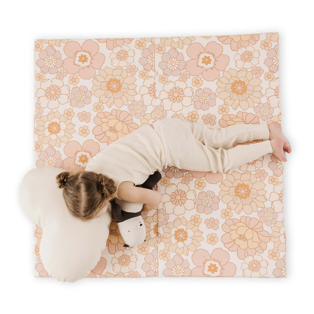 Child laying down on the Toki Mats Vegan Leather Play Mat with pillow and toy  in -- Color_Blooms 