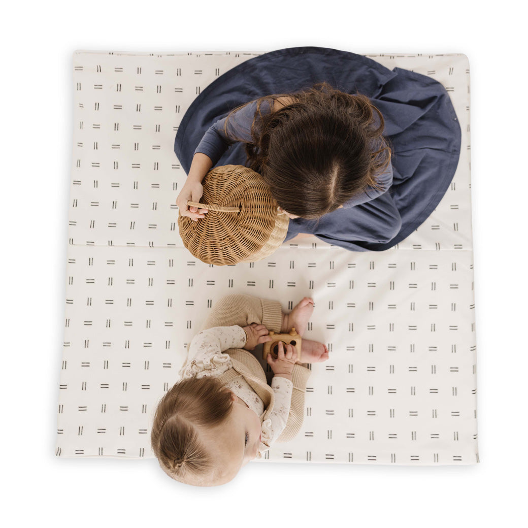 Two kids sitting on the Toki Mats Vegan Leather Play Mat in -- Color_Mudcloth