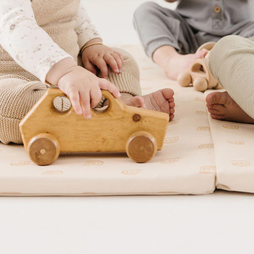 Closeup of kids playing on the Toki Mats Vegan Leather Play Mat in -- Color_Rainbow Stamp in Cream
