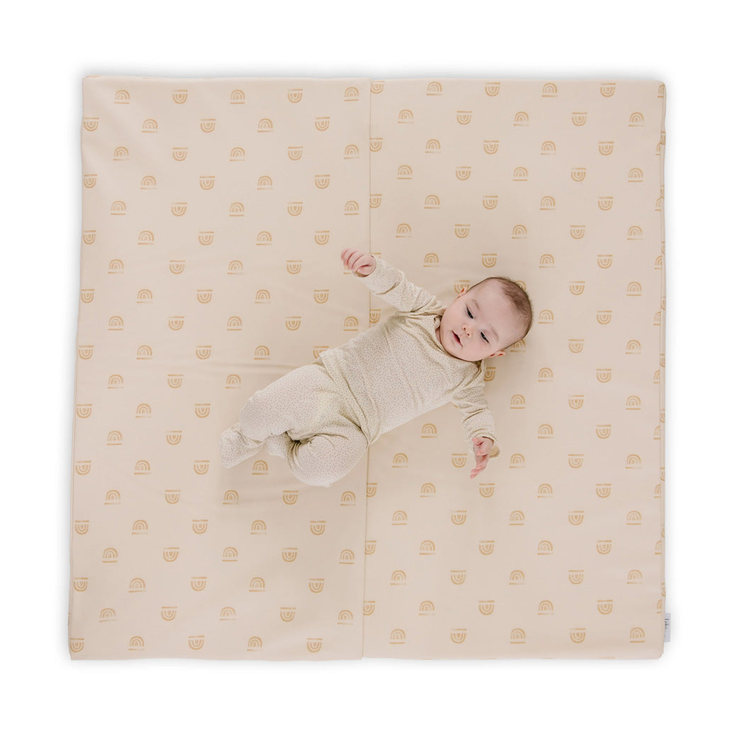 Baby laying on the Toki Mats Vegan Leather Play Mat in -- Color_Rainbow Stamp in Cream