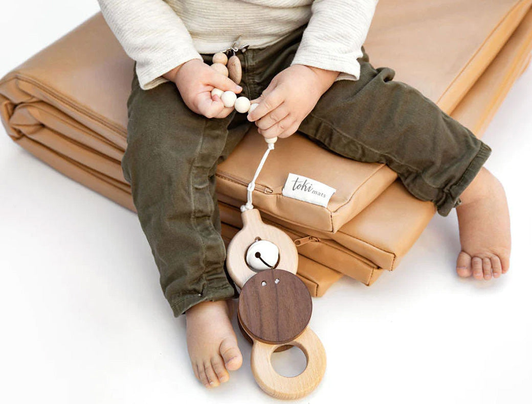 A child sitting on the folded Toki Mats Vegan Leather Play Mat in -- Color_Sand