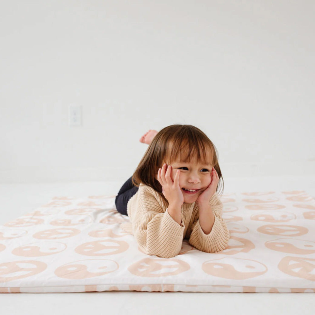 Toddler laying and smiling on the Toki Mats Padded Organic Cotton Play Mat in -- Color_Yin Yang