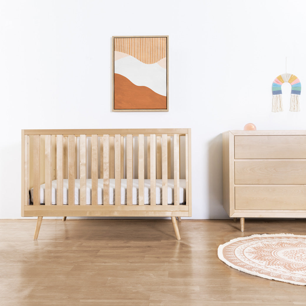 Ubabub Nifty Timber 3-In-1 Crib next to a dresser in -- Color_Natural Birch