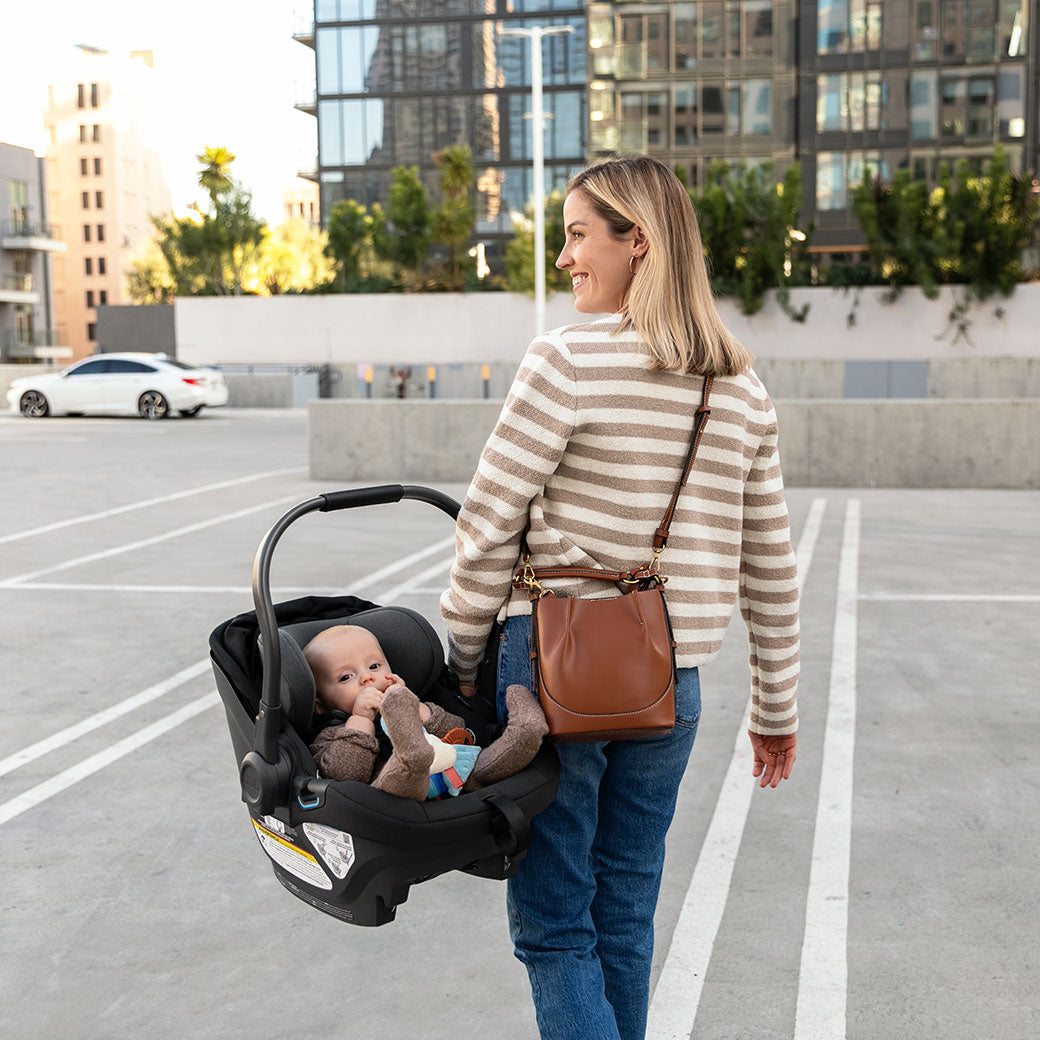 Mom carrying baby in the Uppababy Aria Infant Car Seat in -- Color_Jake
