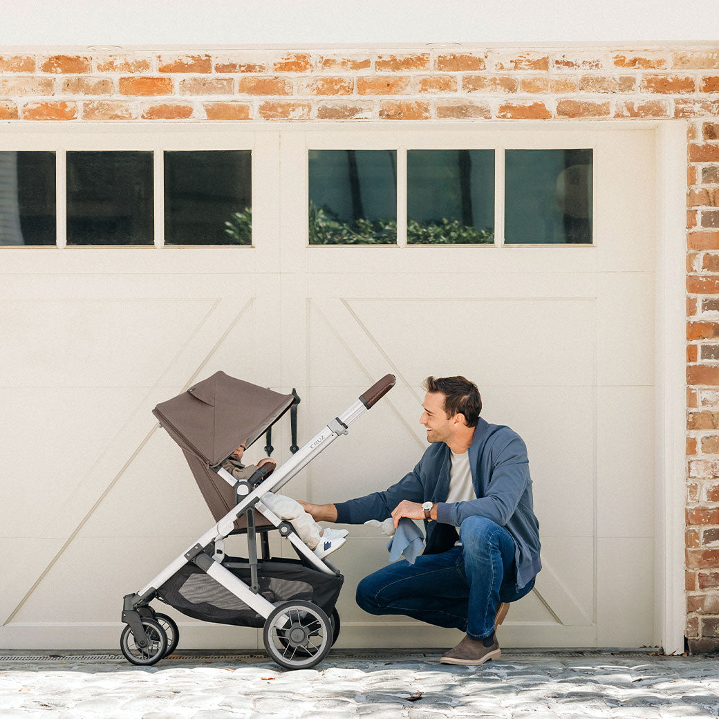 A dad in front of a garage with a baby in the UPPAbaby Cruz V2 Stroller in -- Color_Theo