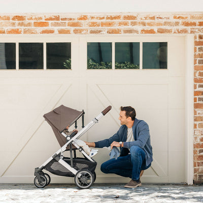 Dad in front of a garage with baby in UPPAbaby CRUZ V2 Travel System stroller in -- Color_Theo