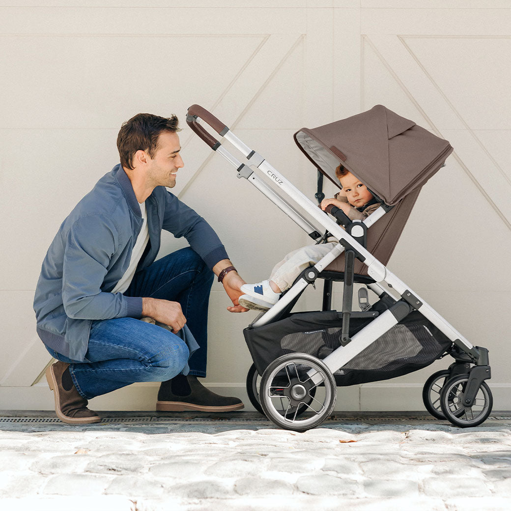 A dad kneeling and looking at a child in the UPPAbaby Cruz V2 Stroller in -- Color_Theo