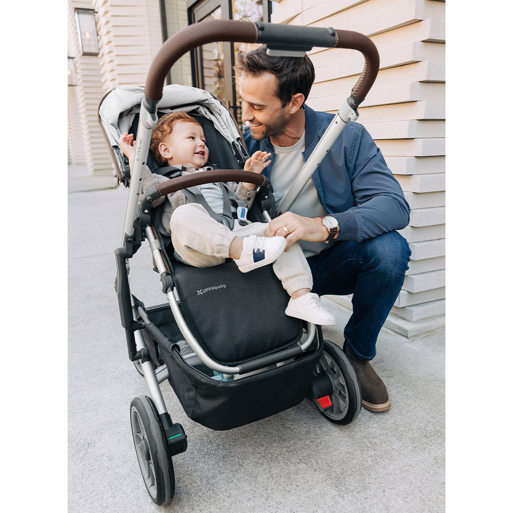 Dad kneeling and looking at baby in the UPPAbaby CRUZ V2 Travel System stroller in -- Color_Theo