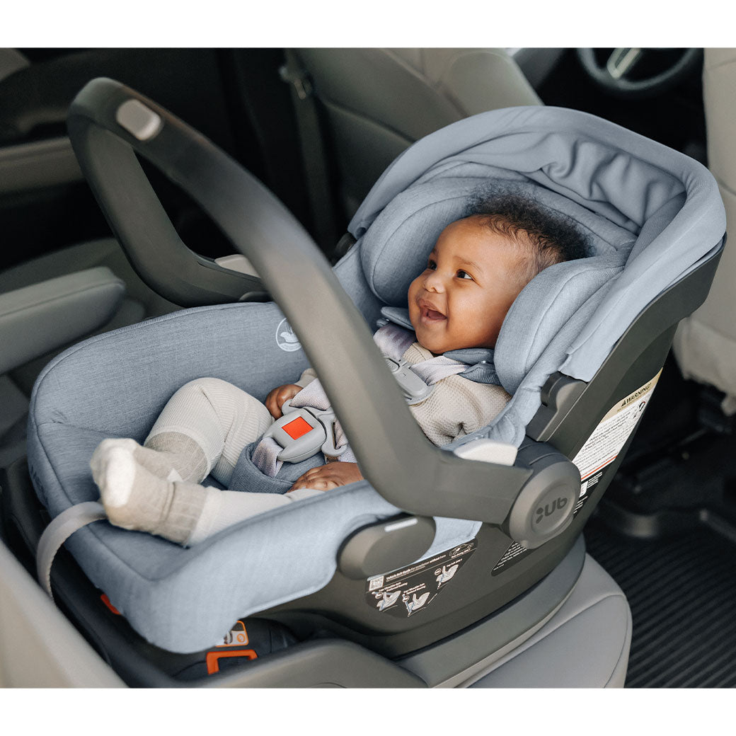 Baby smiling in the back seat of a car in the UPPAbaby MESA V2 Infant Car Seat in -- Color_Gregory