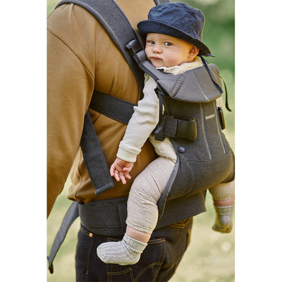 Dad walking with baby on back in the BABYBJÖRN Baby Carrier One in -- Color_Denim Gray/Dark Gray Cotton