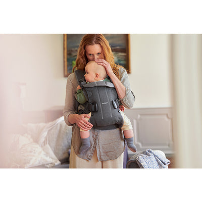 Mother kissing baby in forehead while in BABYBJÖRN Baby Carrier One in -- Color_Denim Gray/Dark Gray Cotton