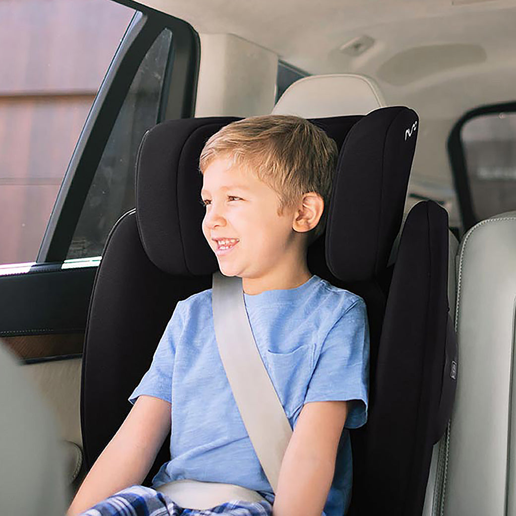 A child looking out the window and sitting in the Nuna AACE Booster Seat in -- Color_Caviar