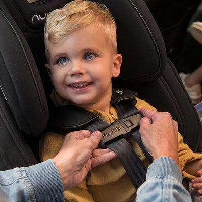 Baby being strapped into the Nuna EXEC Car Seat in Color_Caviar — All
