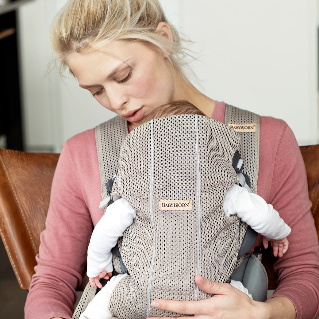 Back view of BABYBJÖRN Baby Carrier Mini with baby in it and mom holding baby in -- Color_Beige Grey 3D Mesh