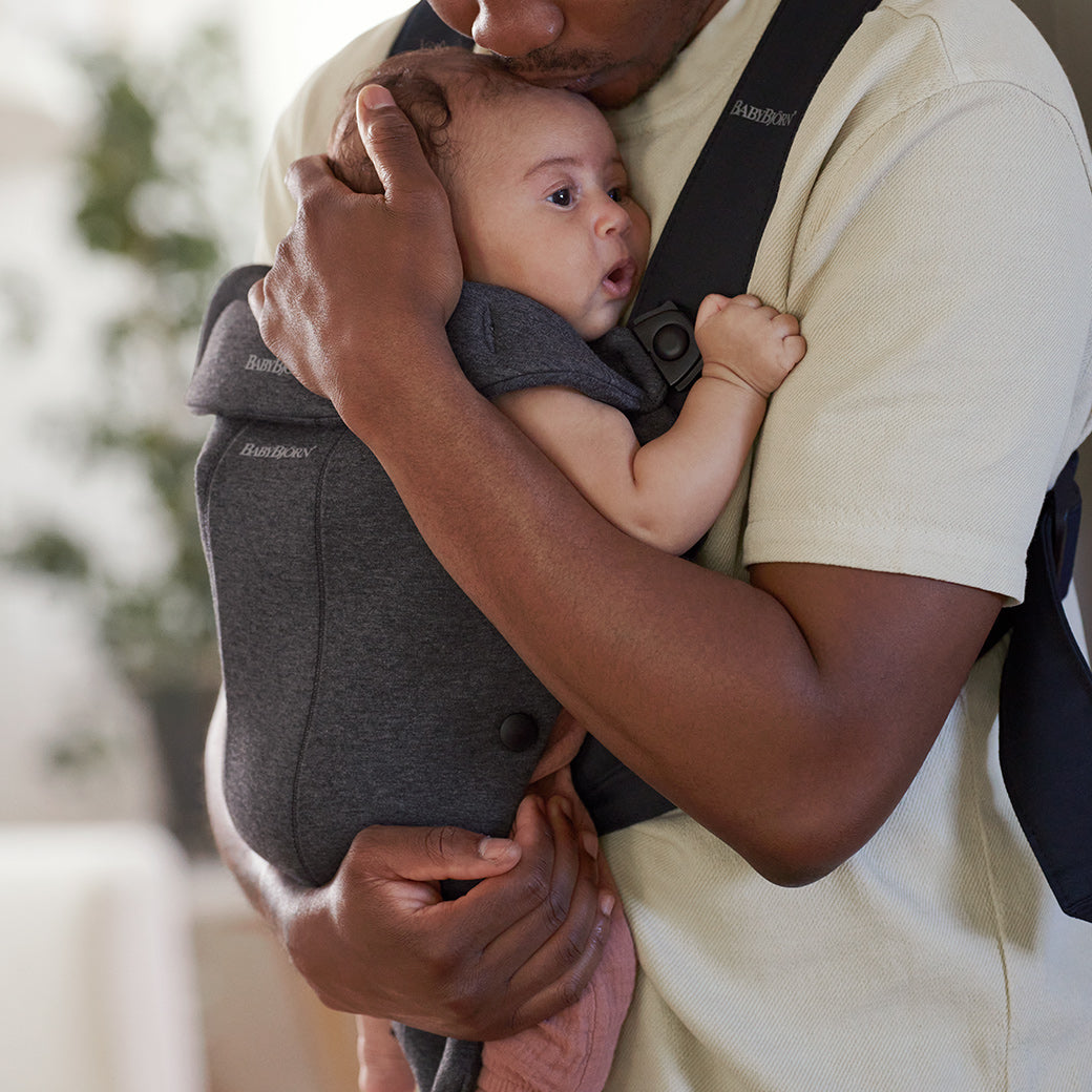 Dad carrying and hugging baby in BABYBJÖRN Baby Carrier Mini in -- Color_Charcoal 3D Jersey