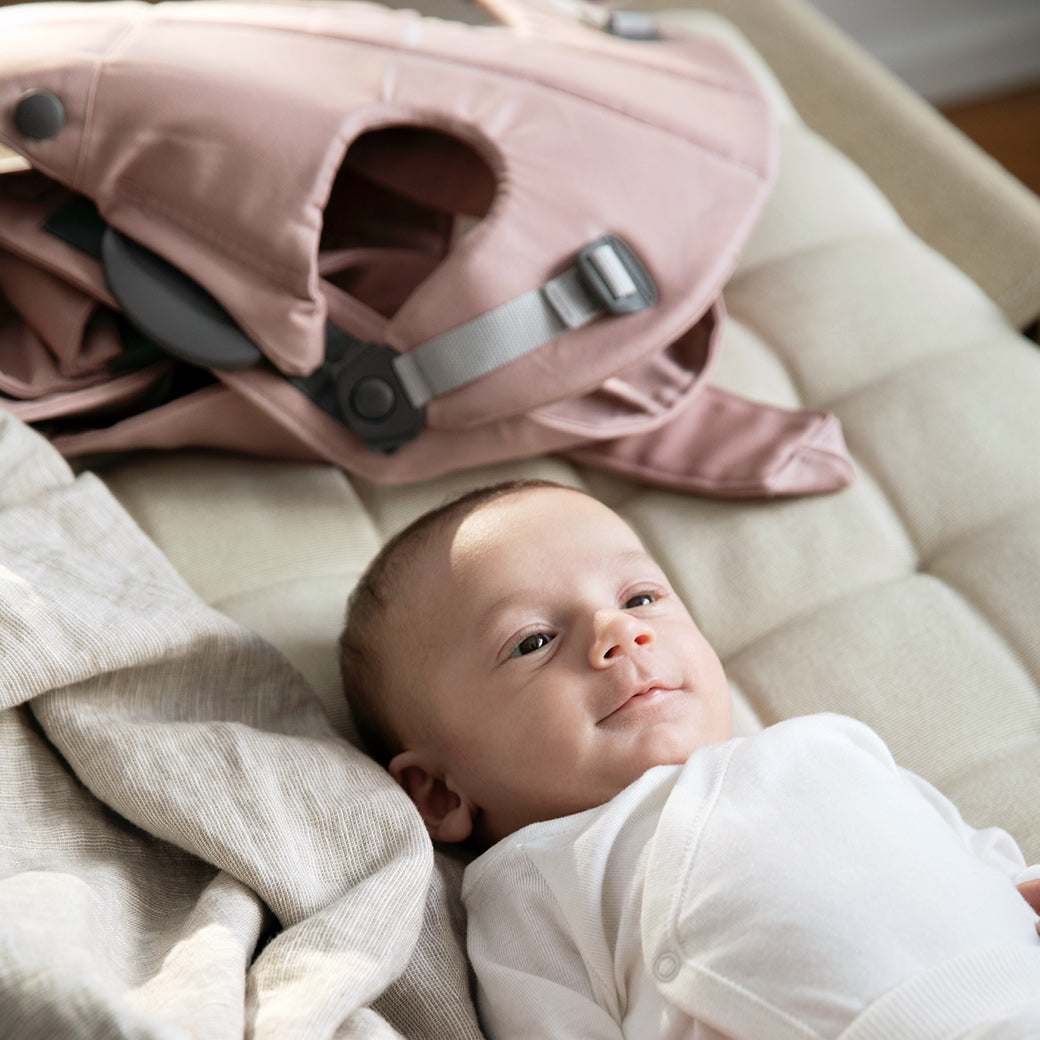 Baby laying next to BABYBJÖRN Baby Carrier Mini in -- Color_Dusty Pink Woven