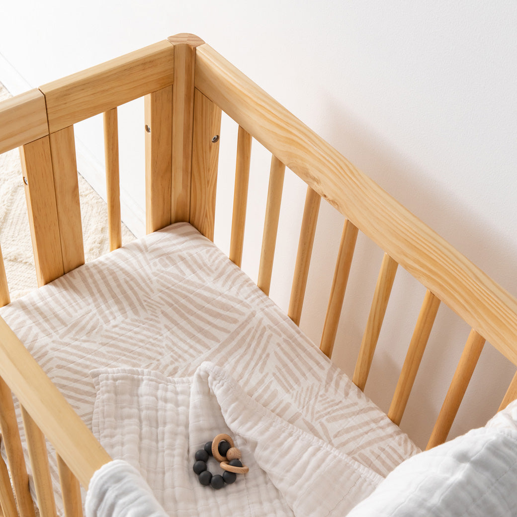 Babyletto All-Stages Bassinet Sheet In GOTS Certified Organic Muslin Cotton in a crib with a toy in -- Color_Oat Stripe