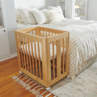 Babyletto All-Stages Bassinet Sheet In GOTS Certified Organic Muslin Cotton in a crib next to a bed  in -- Color_Oat Stripe