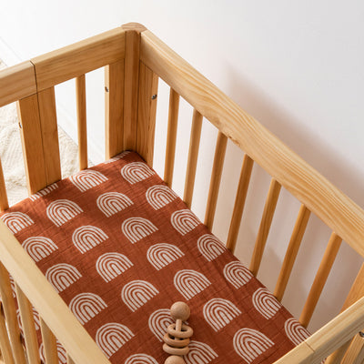 Babyletto All-Stages Bassinet Sheet In GOTS Certified Organic Muslin Cotton in a crib with a toy in -- Color_Terracotta Rainbow