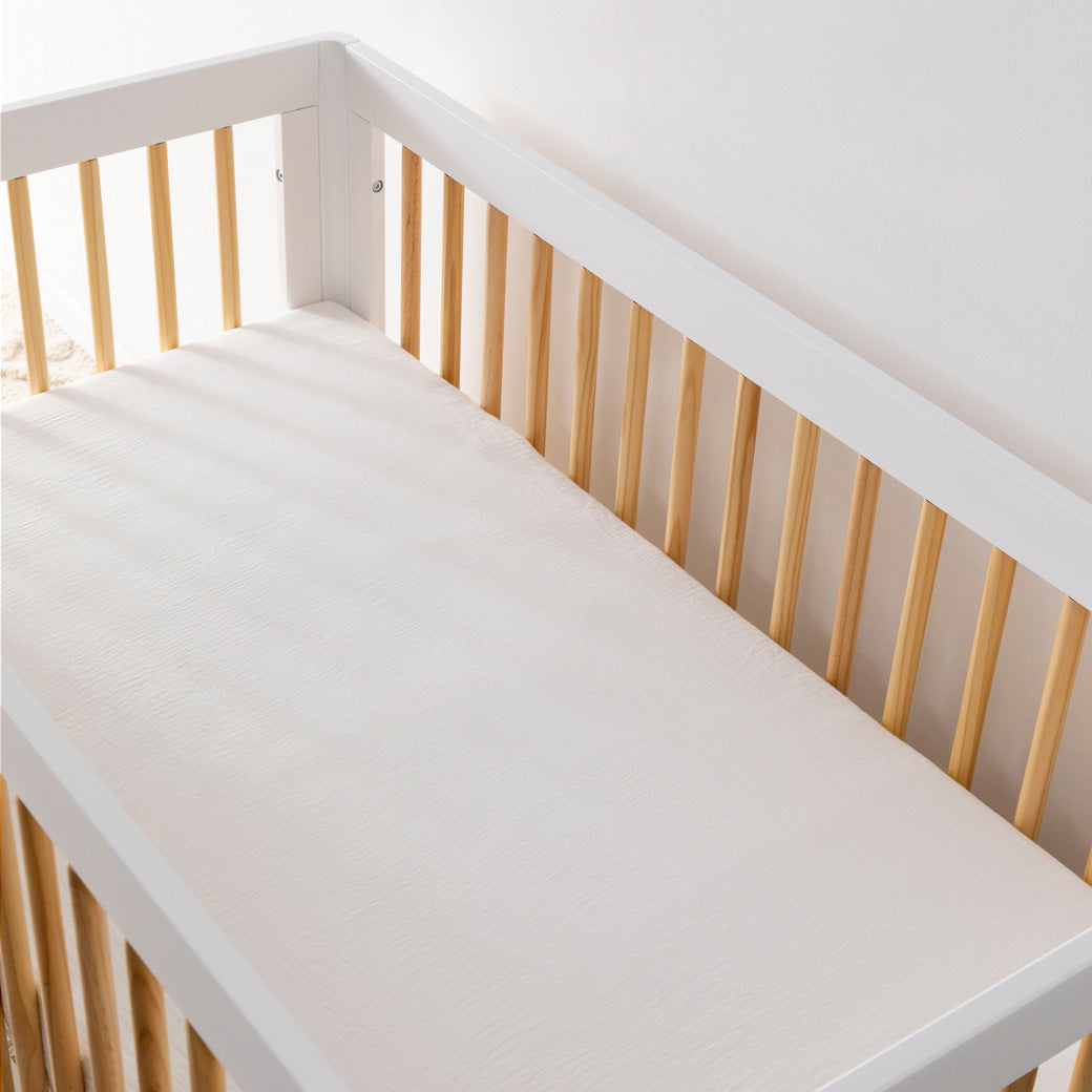 An empty crib equipped with  the Babyletto's Crib Sheet in GOTS Certified Organic Muslin Cotton in -- Color_White
