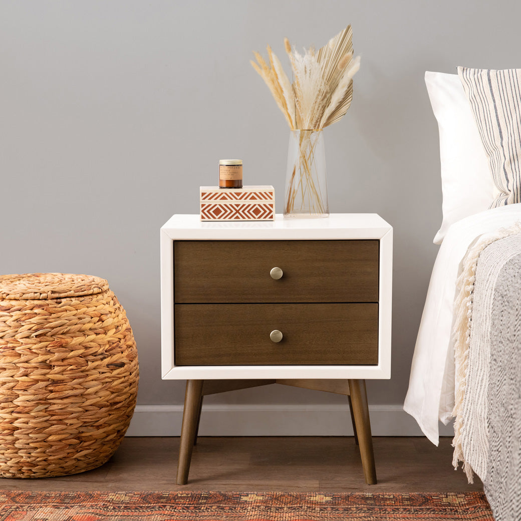 Front view of Babyletto's Palma Nightstand With USB Port next to a basket and bed in -- Color_Warm White with Natural Walnut