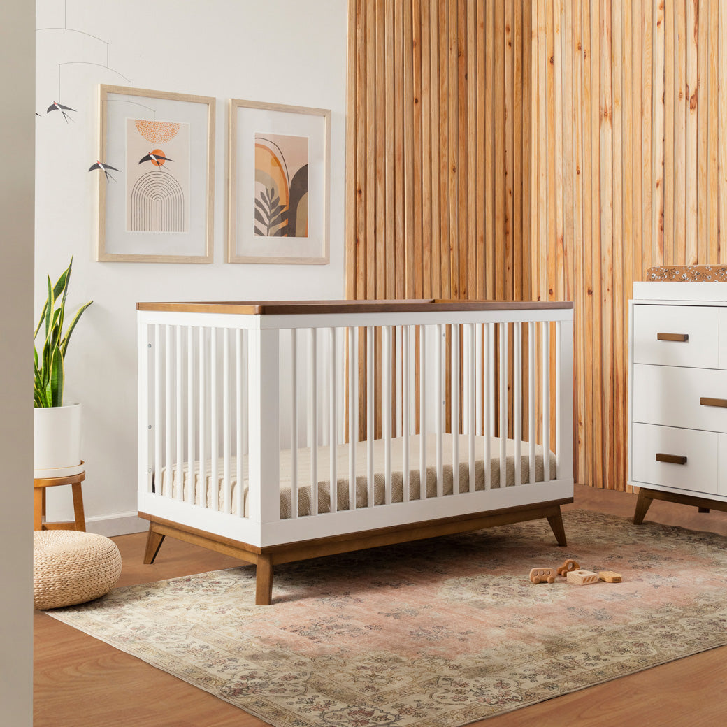 Babyletto's Scoot 3-in-1 Convertible Crib next to a dresser in -- Color_White/Natural Walnut