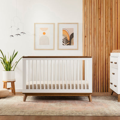 Front view of Babyletto's Scoot 3-in-1 Convertible Crib next to dresser in -- Color_White/Natural Walnut