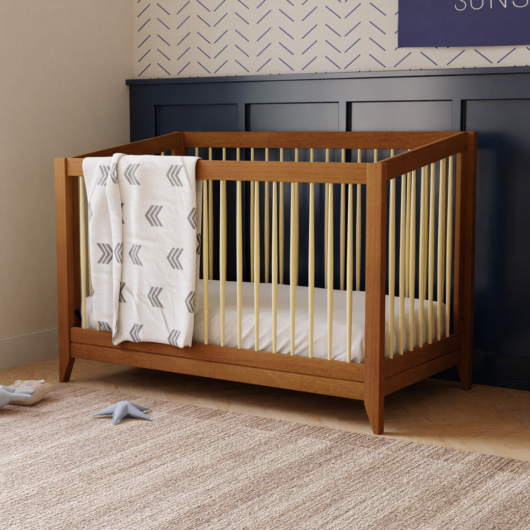 Babyletto's Sprout 4-in-1 Convertible Crib with a blanket over the rail in -- Color_Chestnut / Natural