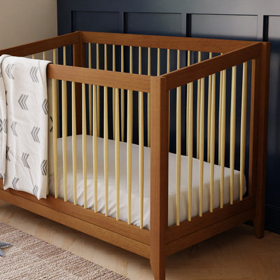 Closeup of Babyletto's Sprout 4-in-1 Convertible Crib with a blanket over the rail in -- Color_Chestnut / Natural