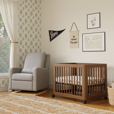 Babyletto's Yuzu 8-In-1 Convertible Crib next to a recliner in -- Color_Natural Walnut