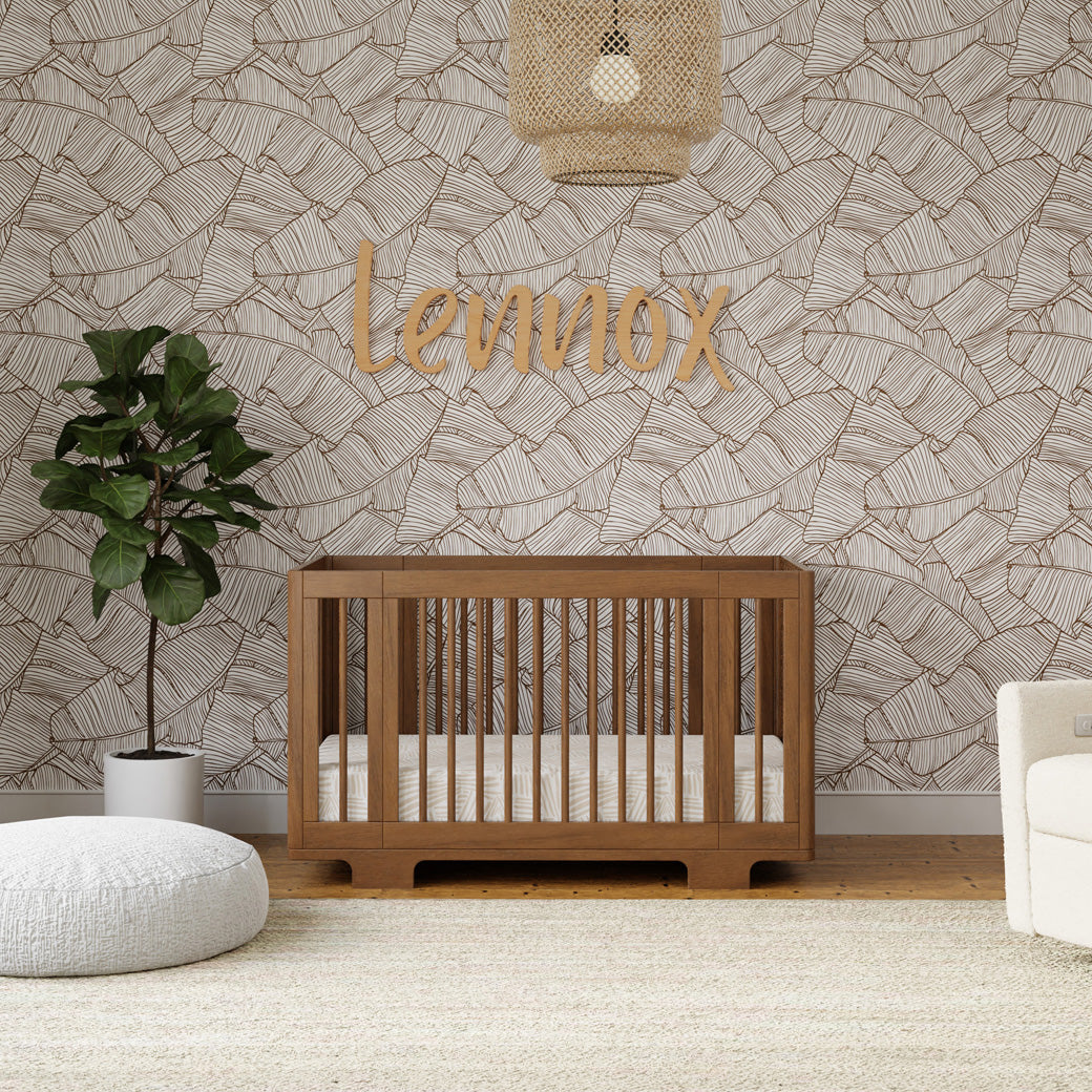 Front view of Babyletto's Yuzu 8-In-1 Convertible Crib next to a plant in -- Color_Natural Walnut