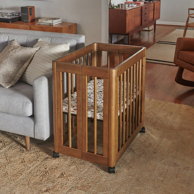 Babyletto's Yuzu 8-In-1 Convertible Crib next to a couch in -- Color_Natural Walnut