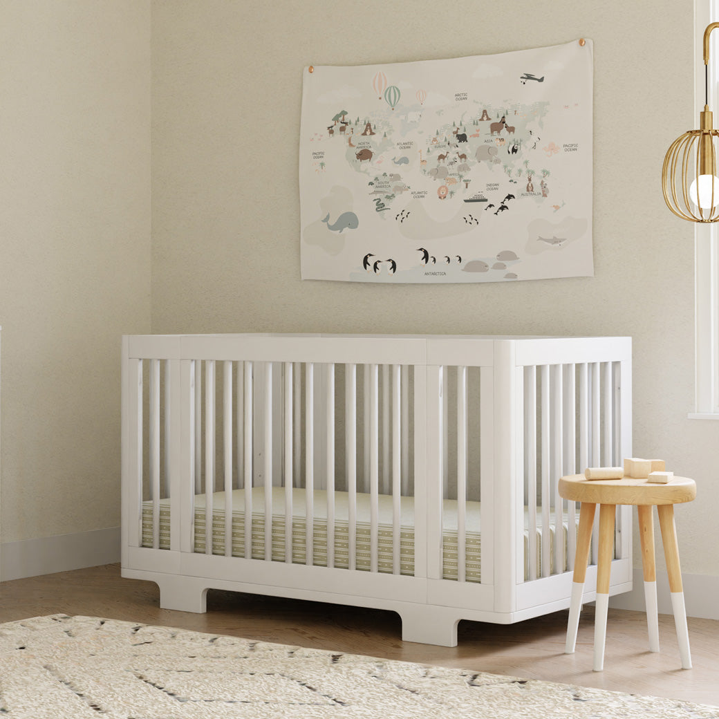 Babyletto's Yuzu 8-In-1 Convertible Crib With All Stages Conversion Kits in a room next to a table in -- Color_White