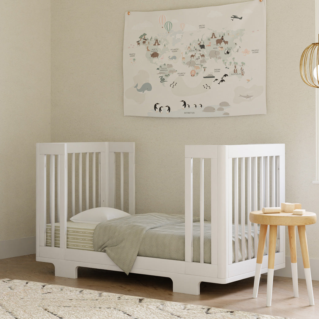 Babyletto's Yuzu 8-In-1 Convertible Crib With All Stages Conversion Kits next to a table as a toddler bed  in -- Color_White