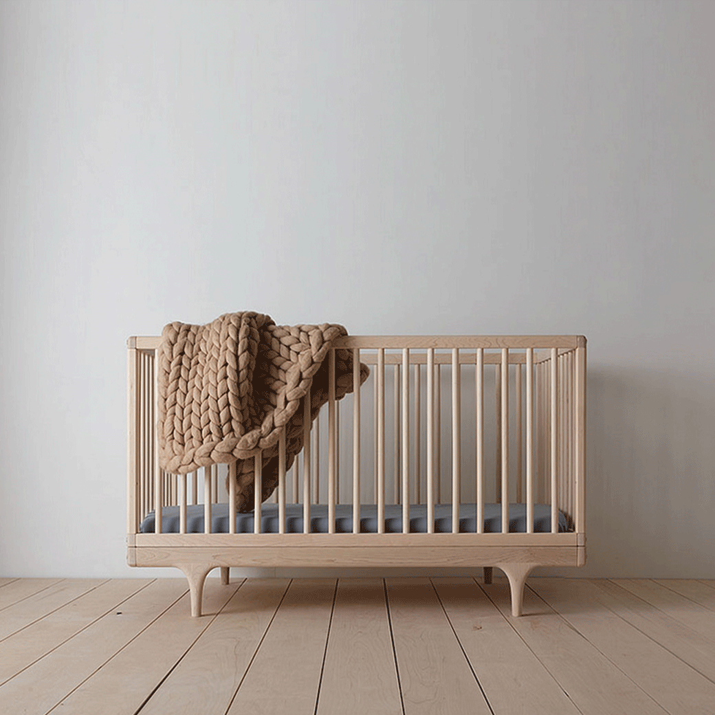 Kalon Caravan Crib with a mattress and a blanket over the rail  in -- Color_Oiled Ash