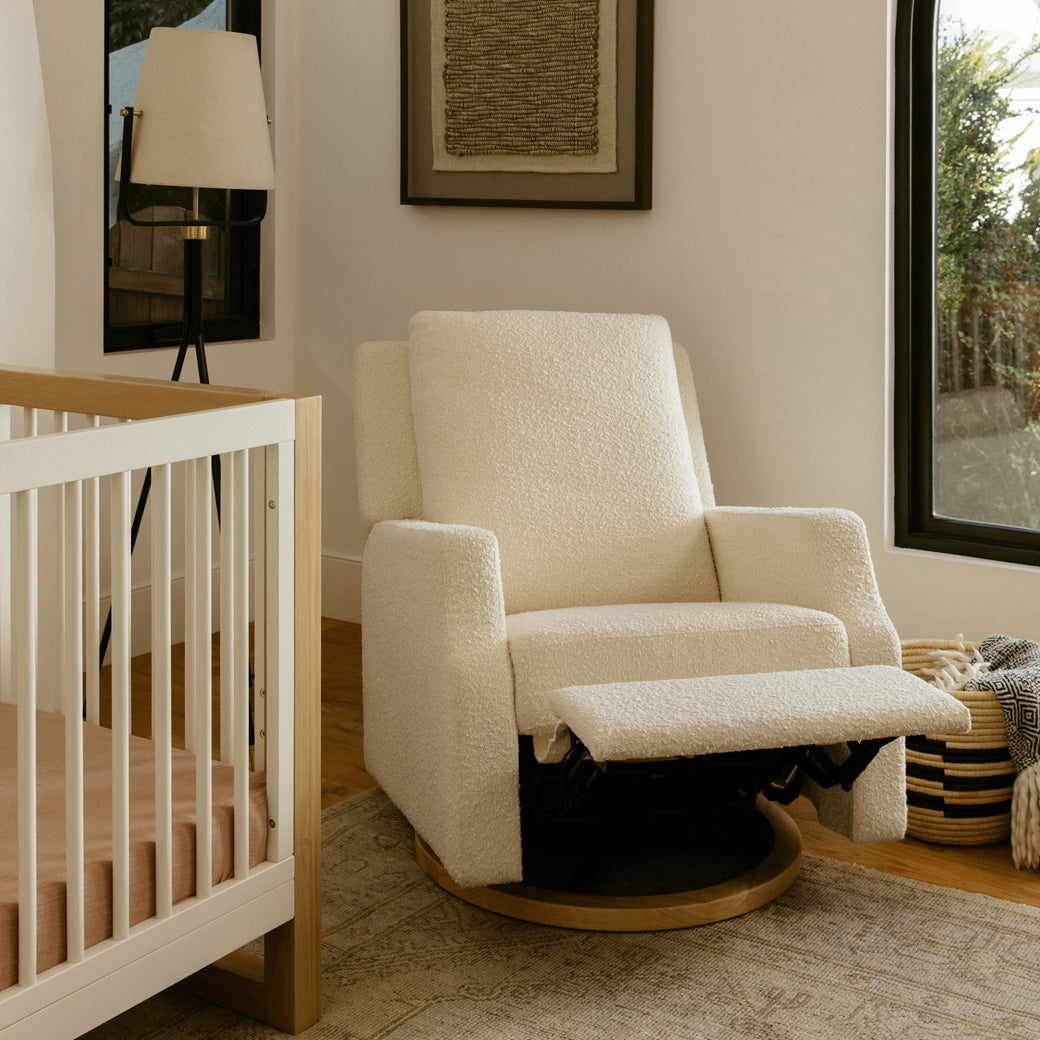 Namesake's Crewe Recliner & Swivel Glider next to a crib and window  in -- Color_Ivory Boucle With Light Wood Base