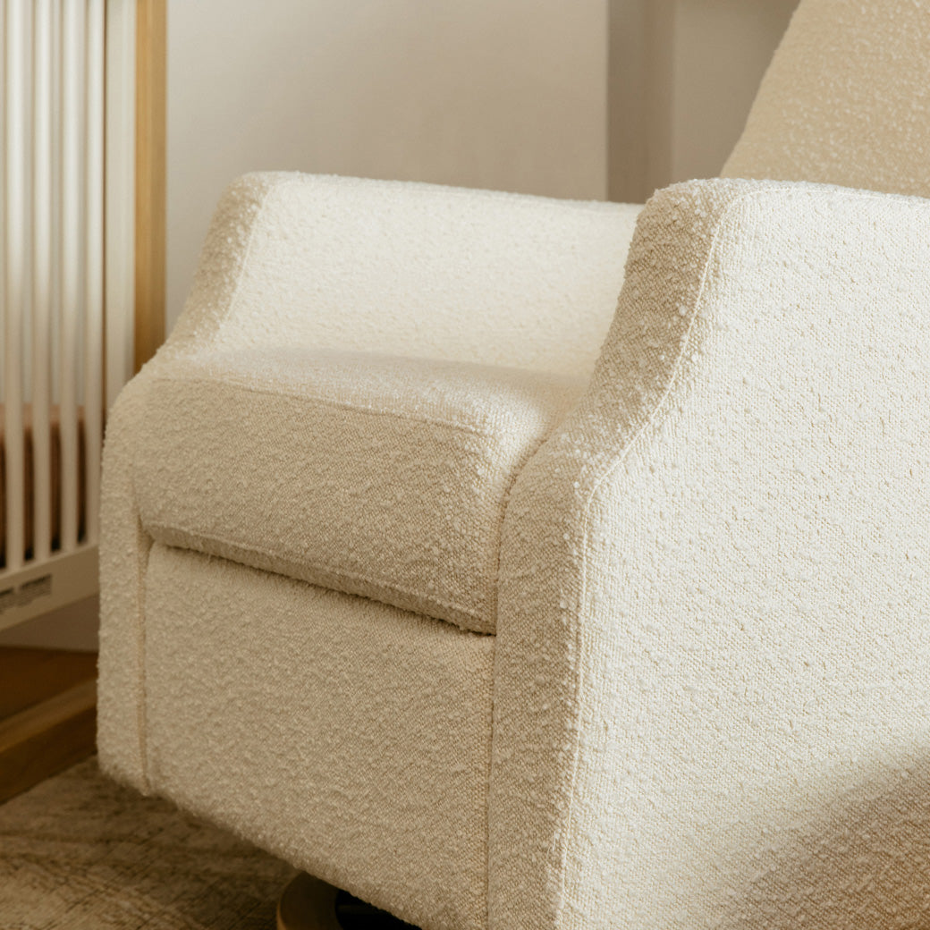 Closeup view of seat of Namesake's Crewe Recliner & Swivel Glider next to a crib  in -- Color_Ivory Boucle With Light Wood Base
