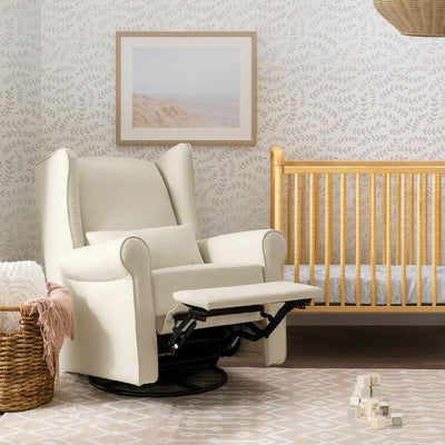 DaVinci Hayden Recliner & Swivel Glider with reclined footrest next to a crib in -- Color_Natural Oat