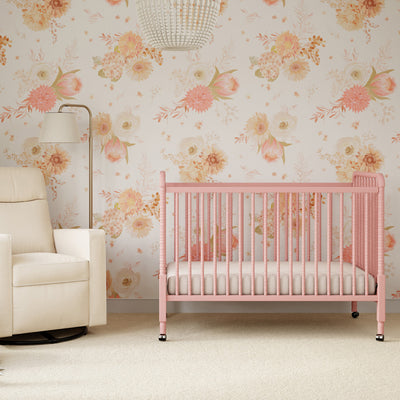 Lifestyle front view of the DaVinci’s Jenny Lind Crib next to a recliner in a floral room in -- Color_Blush Pink