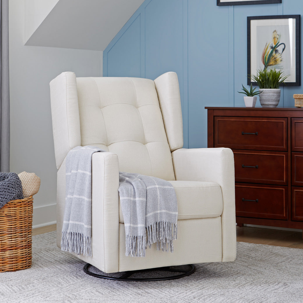 DaVinci's Maddox Recliner & Swivel Glider next to a basket and dresser in -- Color_Natural Oat