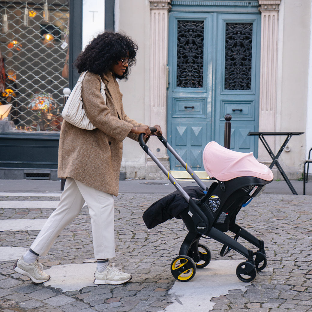 Woman pushing Doona Infant Car Seat and Stroller in Blush Pink on the side walk -- Color_Blush Pink
