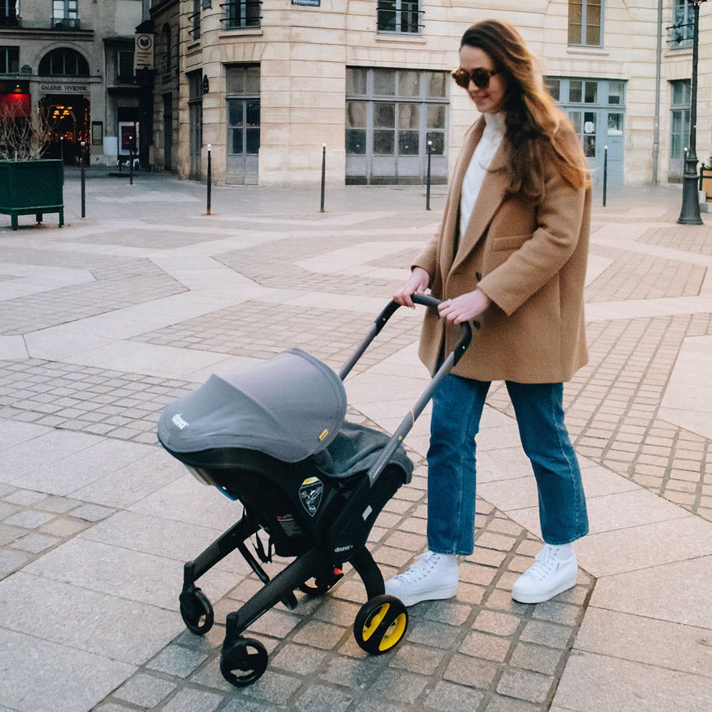 Woman walking with the Doona Infant Car Seat and Stroller in -- Color_Greyhound