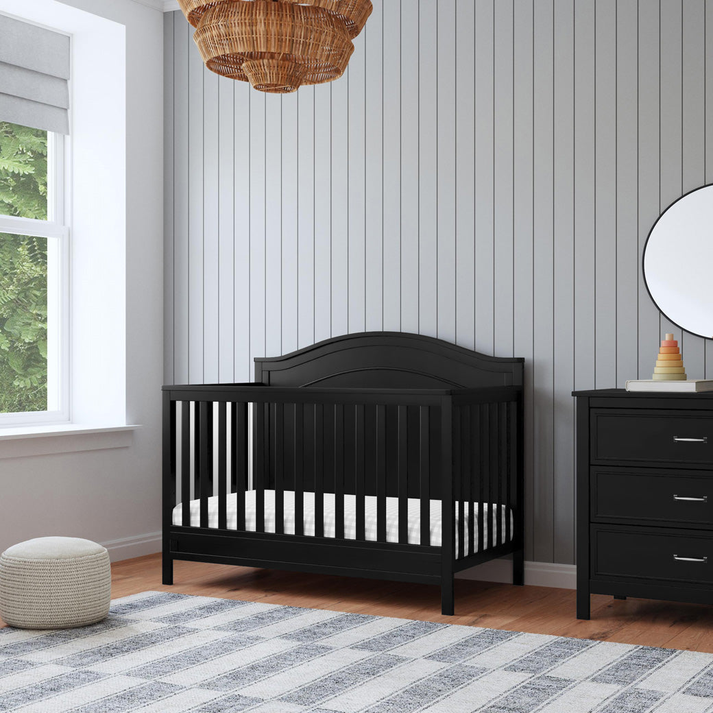 The DaVinci Charlie 4-in-1 Convertible Crib next to a window and dresser  in -- Color_Ebony