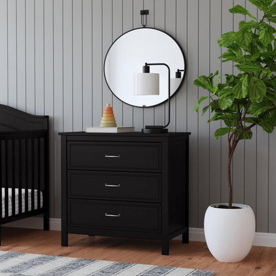 Lifestyle corner view of The DaVinci Charlie 3-Drawer Dresser under a mirror and next to a plant  in -- Color_Ebony